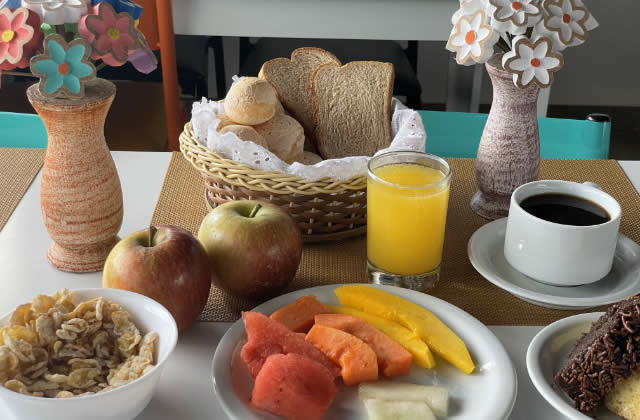 Mesa de café da manhã com frutas, pães, suco de laranja e café