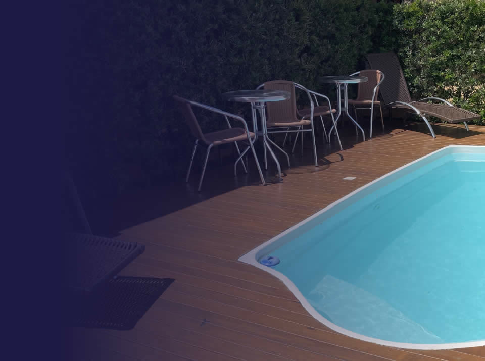 Piscina com deck de madeira, mesas e espreguiçadeira