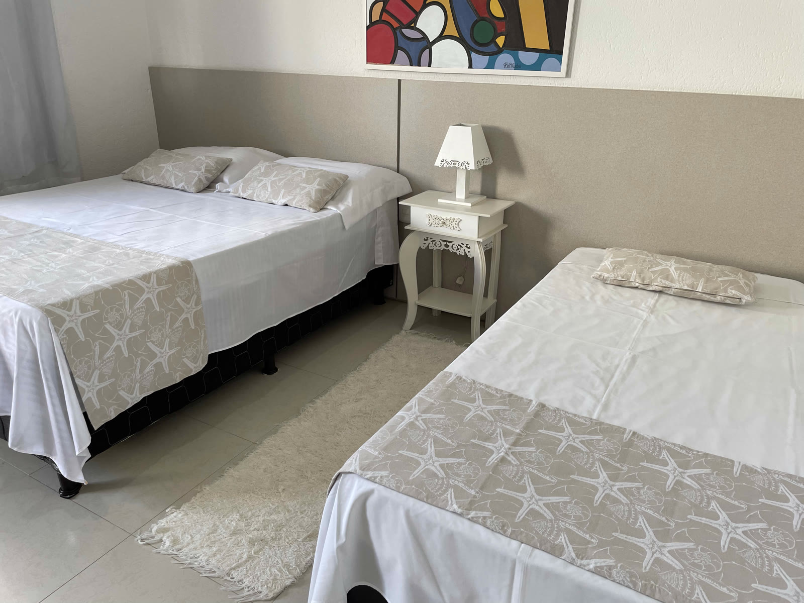 Cama de casal e cama de solteiro arrumadas com colchas de estrela-do-mar, criado-mudo com abajur
