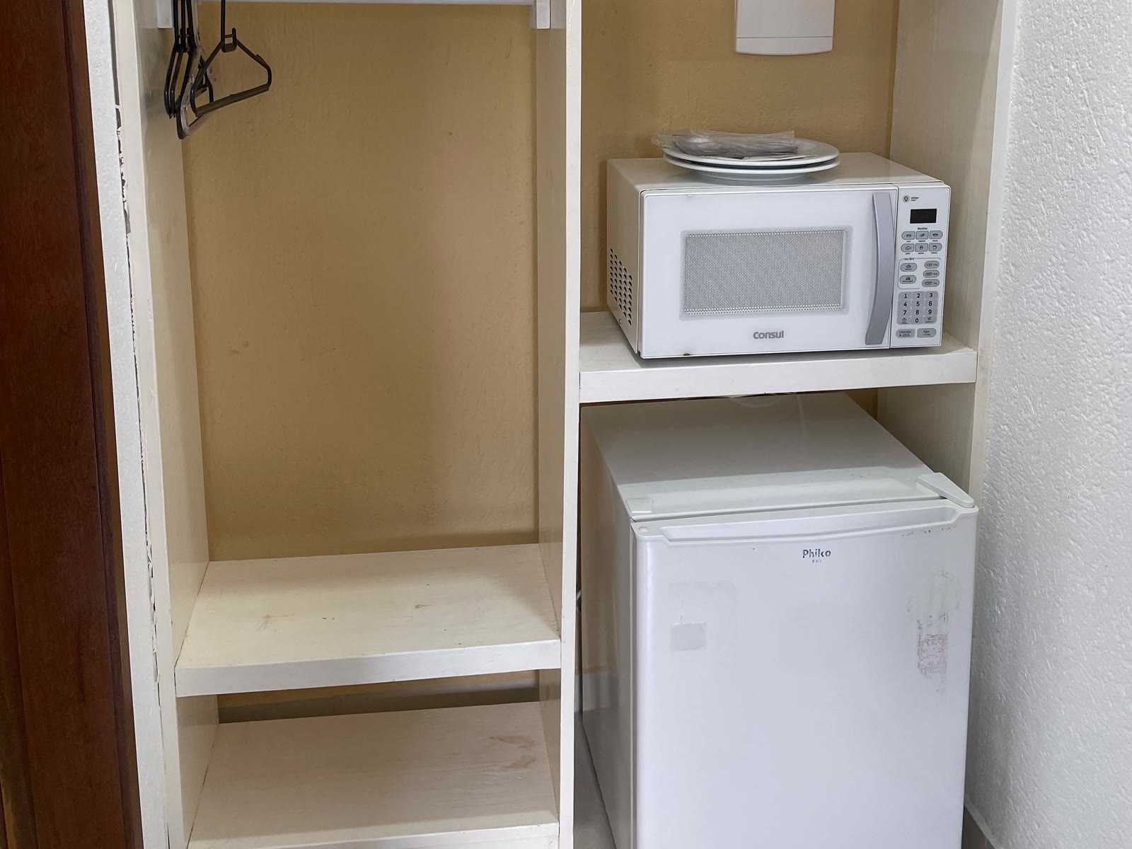 Armário aberto com micro-ondas, pratos e frigobar